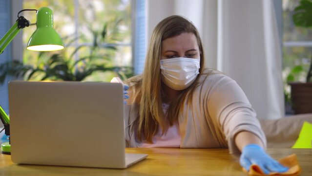 Woman wearing face mask using spray disinfection alcohol sanitizing and wiping workplace. Realtime