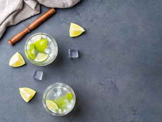 Brazilian lemon caipirinha in glasses with ice and fruit slices over stone background with copy space