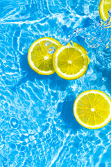 Creative summer composition made of sliced lemon in transparent blue water. Refreshment concept. Healthy refreshing drink theme. Top view - obrazy, fototapety, plakaty