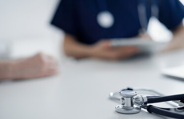 Stethoscope lying on the tablet computer in front of a doctor and patient at the background. Medicine, healthcare concept.