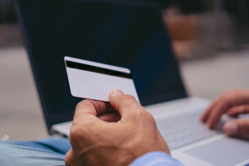 Hand of a man holding a credit card and interacting with his laptop in the background.