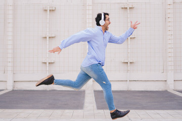 Latin man with headphones and casual clothes running with a happy face.