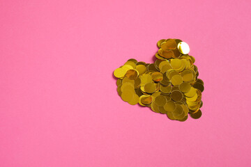 golden confetti laid out in a heart shape on a pink background