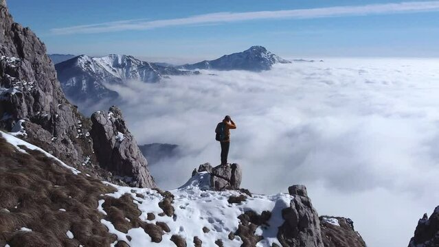 Hiker standing on mountain top over clouds with arms outstretched