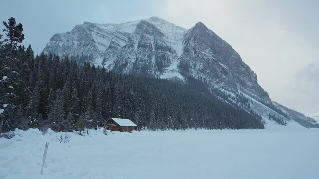 Scenery of Lake Louise with wooden cottage glowing and rocky mountains with snowfall in winter at Banff national park