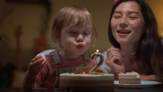 Small family celebrating son birthday at home. Dad and mom whistle a pipe smile clapping hands together. Excited little boy looking at cake with burning candles. Happy kid blow candles and make a wish
