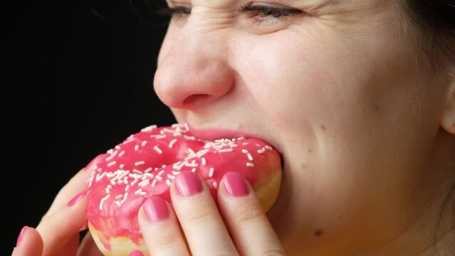 A woman eats a delicious red doughnut, bites and chews it appetizingly, close-up. High-calorie sweet food, diabetes