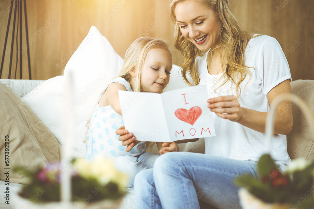 Wall mural happy mother day in sunny flat. child daughter congratulates mom and gives her postcard with heart d