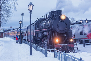 Retro steam train arrives to the station platform at winter evening.