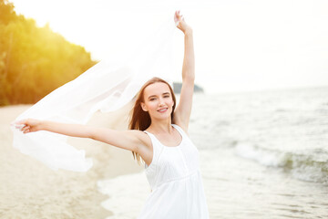 Fototapeta na wymiar Happy smiling woman in free happiness bliss on ocean beach catching clouds. Portrait of a multicultural female model in white summer dress enjoying nature during travel holidays vacation outdoors.