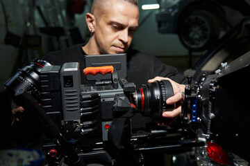 Fototapeta na wymiar young caucasian male videographer changing lenses on a professional movie camera on set