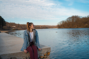Young woman sits on the shore of the lake, enjoying in her free time.