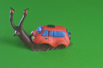 A brown plasticine snail crawls on a green background instead of a house on her back a small red...