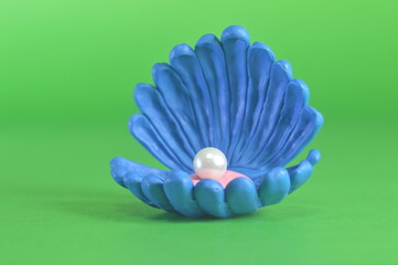 On a green background lies a plasticine figure of a sea shell in the center of which lies a real...