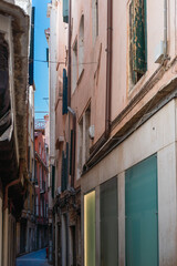 Fototapeta na wymiar View of a narrow street in Venice with a strip of blue sky in the background on a sunny day, old vintage walls of authentic houses, Italian medieval architecture, Venice culture, tourist attractions