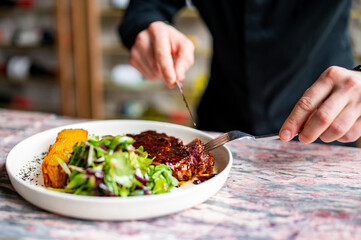 man hands with fork and knife eating beef steak and salad in cafe