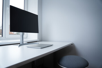 Stylish workplace  with modern gadgets. Emty Workspace for IT specialist. Remote job. Laptop and big screen on a desk. Close-up of closed laptop on white table against the window. 