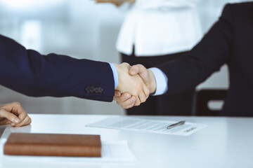 Business people shaking hands at meeting or negotiation, close-up. Group of unknown businessmen, and a woman on the background in a modern office. Teamwork, partnership and handshake concept.