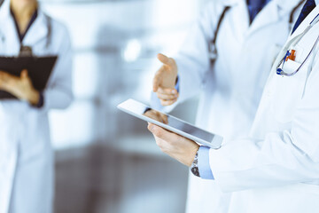 Group of doctors are checking medical names on the computer tablet, when a nurse with a clipboard is making some notes, while standing together in a hospital office