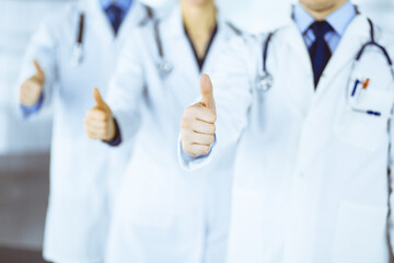 Group of unknown doctors stand as a team with thumbs up in a hospital office. Physicians ready to examine and help patients. Medical help, insurance in health care
