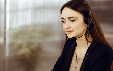 Two young people in headsets are smiling and talking to the clients, while sitting at the desk in a modern office. Call center operators at work