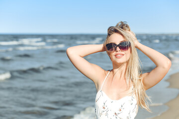 Happy blonde woman in free happiness bliss on ocean beach standing with sun glasses and posing.