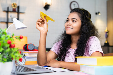 girl holding paper plane dreaming about foreign or abroad study while reading or preparing for examination - concept of future career, imagination and education © WESTOCK