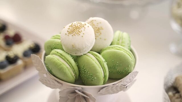 White bowl with green pistachio macarons, matched with white macarons, placed on a white table at a wedding reception