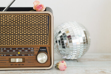Close-up of a vintage retro radio against a light wall on a wooden table, in the background a glass disco ball and buds of dried pink roses, copy space.