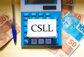A sigla CSLL escrita em um pedaço de papel que está sobre uma calculadora. Notas do Real...