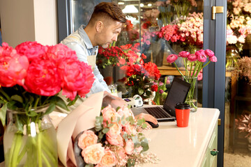 happy middle aged man businessman standing in an apron in a small flower center and writing down order details. Joyful male florist calling by smartphone at work. Own business concept
