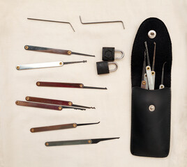 Many lock picking tools in a case, tension wrenches and 2 little padlocks flat lay. A kit of lock picks that can be used by a locksmith for opening doors or burglary