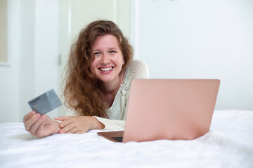 Portrait of happy girl, young positive pretty woman paying, holding credit bank card with phone, laptop. Online shopping at home in living room. Bank application, app.