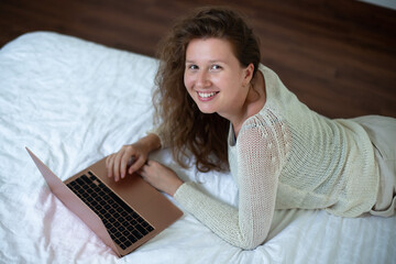 Happy joyful woman is using laptop computer at home on bed in bedroom and smiling 