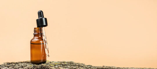 Open amber glass bottle with pipette on natural wood on beige background. The concept of natural, organic cosmetics. Banner with space for text.