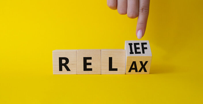 Relief and relax symbol. Businessman points at turned wooden cubes with words Relief and Relax. Beautiful yellow background. Businessman hand. Business and Relief and relax concept. Copy space