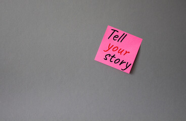 Tell your story symbol. Concept words Tell your story on pink steaky note. Beautiful grey background. Business and Tell your story concept. Copy space.