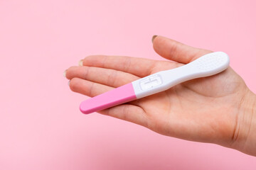 Female hand holding a pregnancy test on the pink background with copy space. 