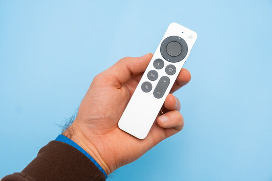 Mans hand holding Siri Apple TV remote controller on the blue background, February 2023, Prague, Czech Republic