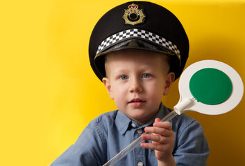 Cute boy in a cap of a policeman showing a green traffic light on a yellow background