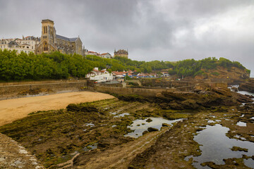 Fototapeta na wymiar View of the beach of the fishing port at low tide, showing us its rocks and the church of Saint Eugénie in the background. Biarritz, France.