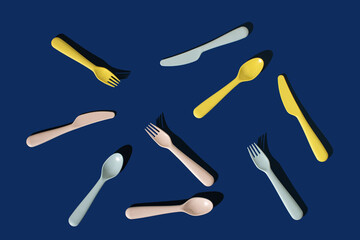 Set of plastic spoons, knives, forks on a blue background. Minimal horizontal flat lay composition, funny fast food serving concept