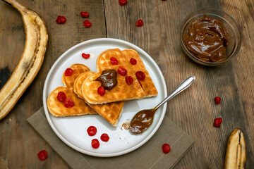 Homemade Belgian waffles heart shaped on plate with colorful red sweet cherry berries, banana, and...