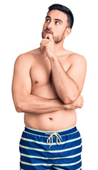 Fototapeta premium Young handsome man wearing swimwear with hand on chin thinking about question, pensive expression. smiling with thoughtful face. doubt concept.