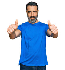 Fototapeta premium Middle aged man with beard wearing casual blue t shirt approving doing positive gesture with hand, thumbs up smiling and happy for success. winner gesture.