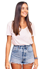 Obraz premium Young hispanic woman wearing casual white tshirt looking away to side with smile on face, natural expression. laughing confident.