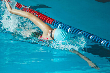 The theme of sports and endurance. Side view of a professional female swimmer with goggles at the pool. A woman swimmer dives into a pool of water. The girl swims underwater in a large pool.