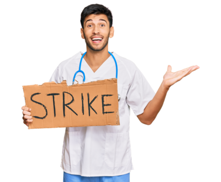Young handsome man wearing doctor uniform holding strike banner cardboard celebrating victory with happy smile and winner expression with raised hands