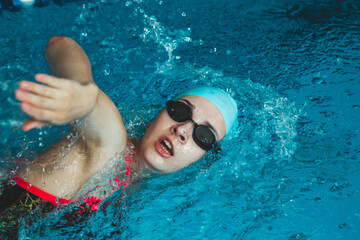 The theme of sports and endurance. Side view of a professional female swimmer with goggles at the pool. A woman swimmer dives into a pool of water. The girl swims underwater in a large pool.