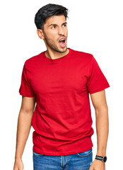 Obraz premium Young handsome man wearing casual red tshirt angry and mad screaming frustrated and furious, shouting with anger. rage and aggressive concept.